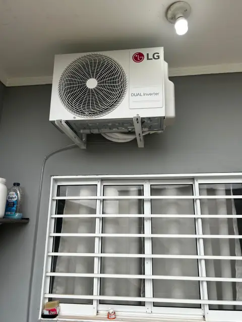 Instalação de ar-condicionado feita pela AF Ar Condicionado: Condensadora LG Dual Inverter em área de serviço, acima de janela com grade.